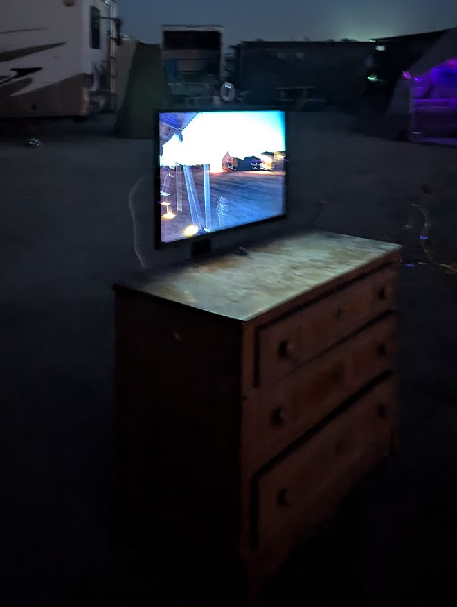 A monitor over a chest of drawers, at night.